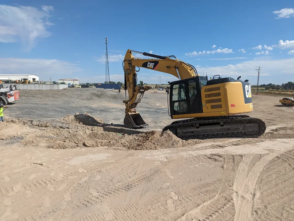 A Cat excavator working a dirt pad on an open commercial site, blue sky overhead