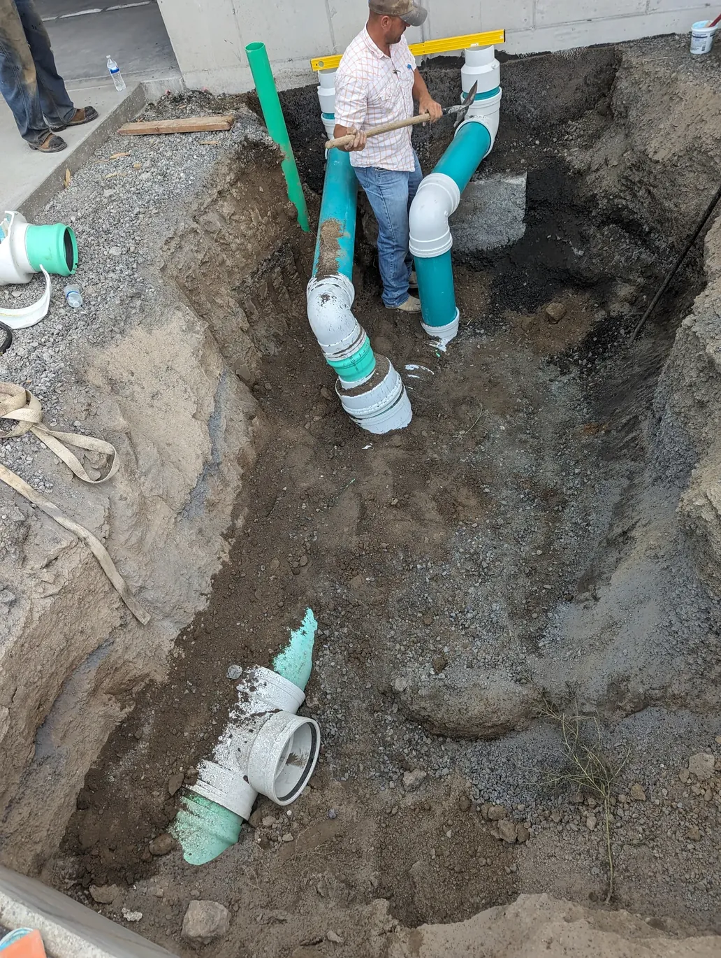 A Dimond crew member installing green PVC sewer and drain piping in an open utility trench at a foundation